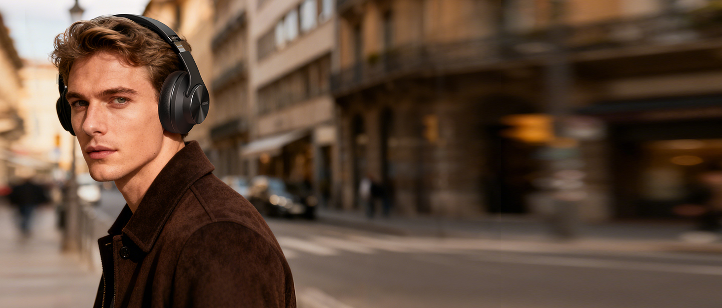 Person wearing over-ear headphones in brown leather jacket against blurred urban background with warm lighting.