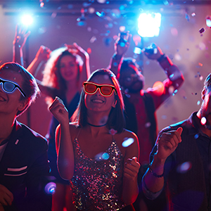Crowded nightclub scene with colorful lights and confetti. People dancing and celebrating in foreground, blurred background.