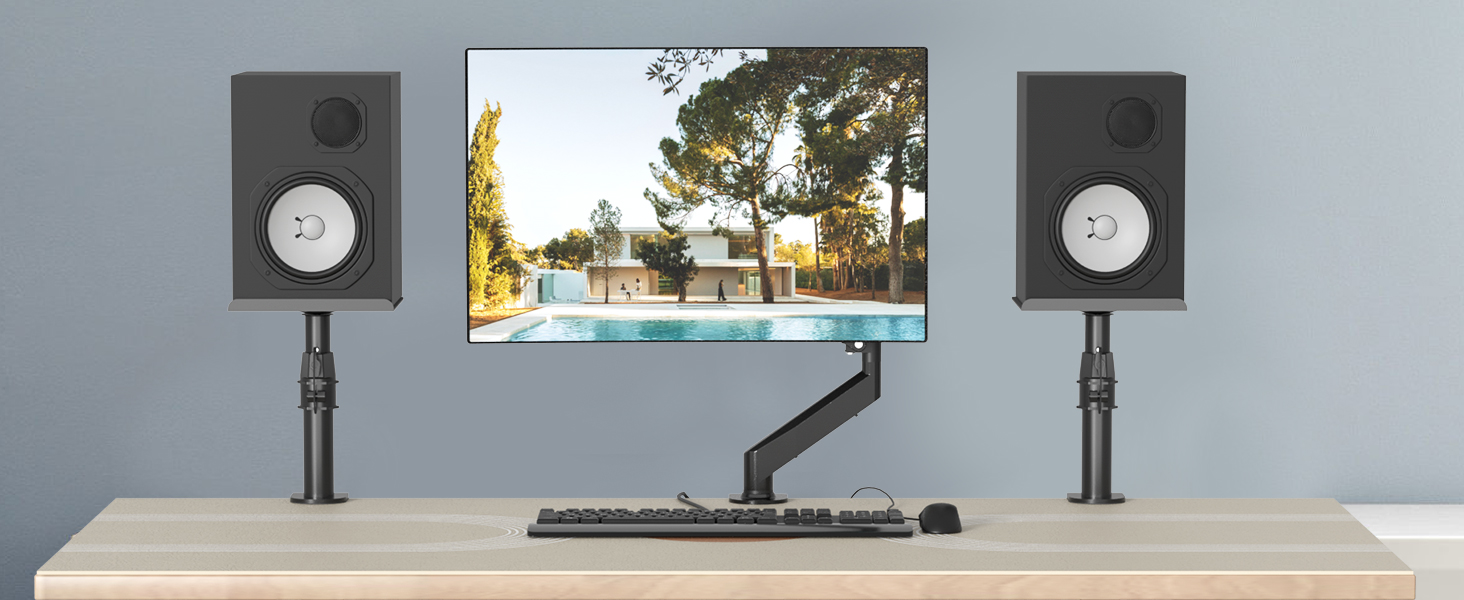 Desktop workstation featuring dual speaker setup with monitor mounted on an articulating arm, positioned on a light-colored desk surface.