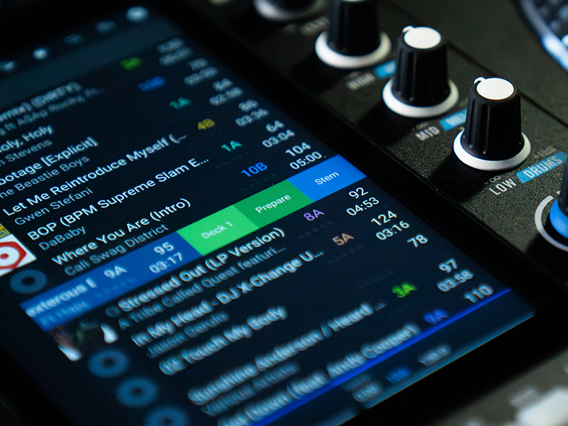 Close-up of audio equipment control panel with blue illuminated display showing digital parameters, white and black knobs, and green level indicators on dark interface.