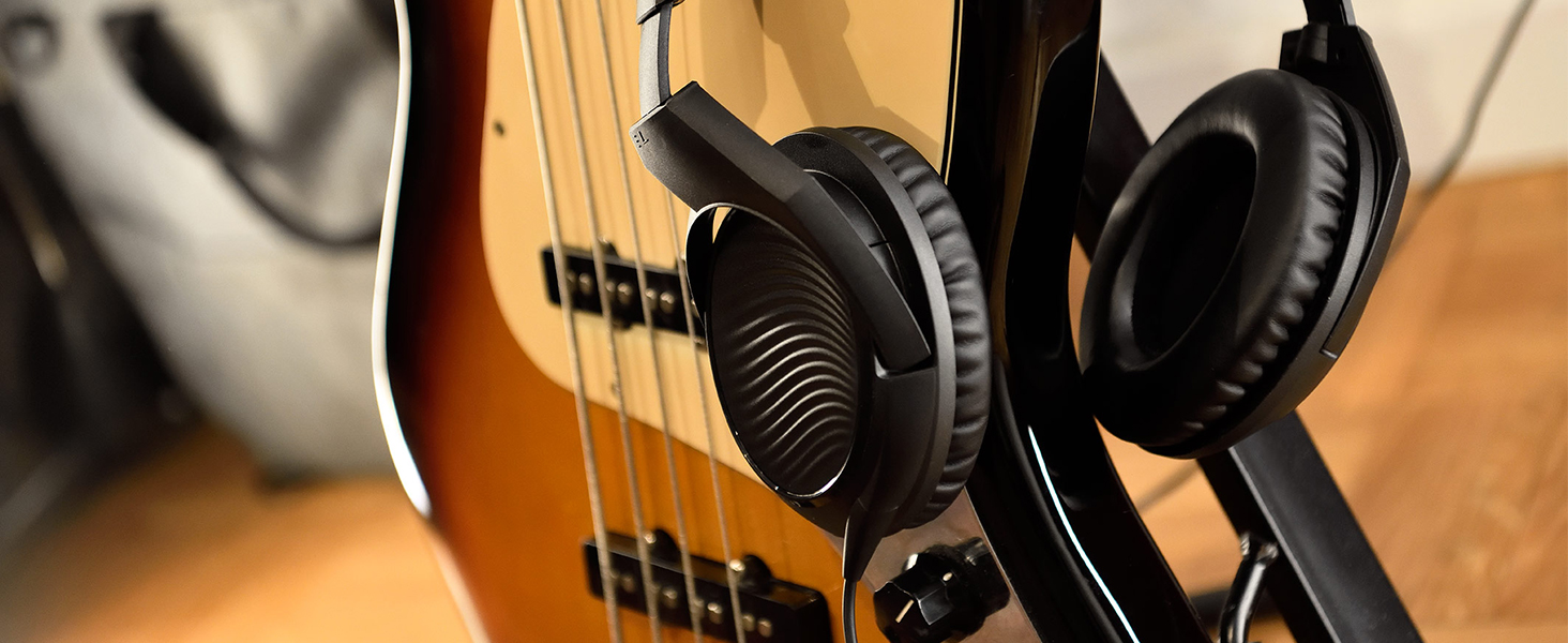 Detailed shot of professional headphones resting on bass guitar strings, highlighting the padded ear cup design and guitar's wood finish.