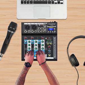 Audio setup with mixing console, microphone, laptop, and headphones on wooden surface. Hands adjusting mixer controls.