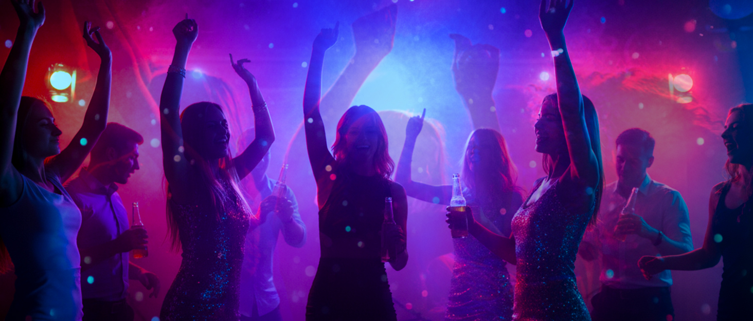 Nightclub or concert scene with silhouettes of people dancing amid purple and pink lighting effects.