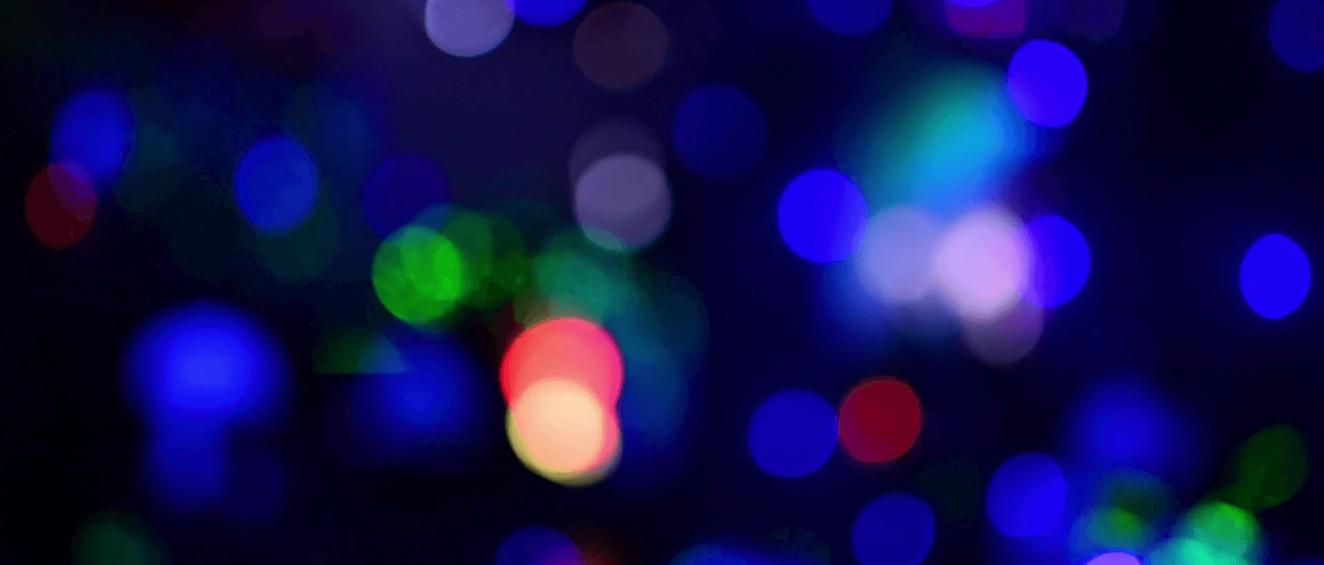 Blurred, out-of-focus image with multiple colored light spots, predominantly blue, against a dark background.