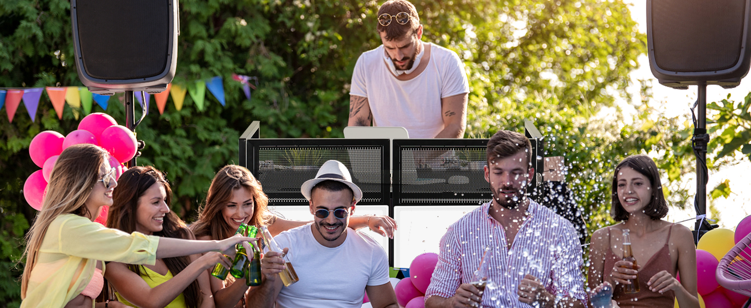 Outdoor party scene with people celebrating around a DJ booth. Colorful flags and speakers visible.