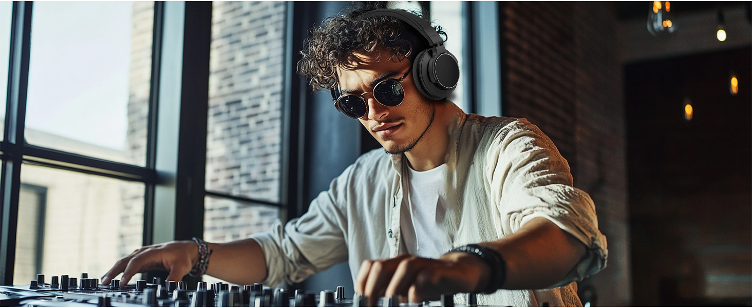 DJ using turntables and mixer, wearing sunglasses and over-ear headphones. White shirt, focused on equipment in a room with brick walls and windows.